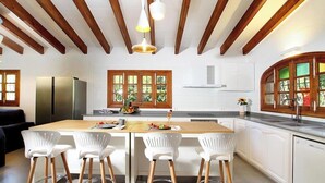 A modern kitchen with wooden beams, white cabinetry, and a central island with bar stools. - Finca Romana by Vida Villas, Fabulous 6 bedroom Villa, Sleeps 12 (Pollença)