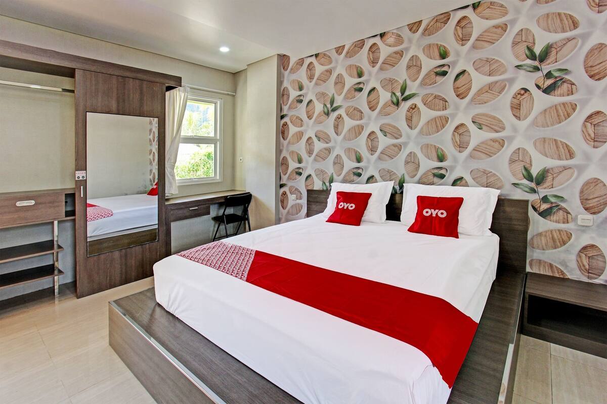 A hotel room with a bed, a desk, a mirror, and a wall with a leaf pattern.