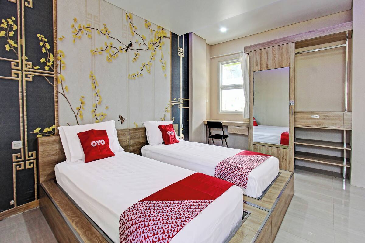 A hotel room with two beds, a desk, a chair, and a large mirror.