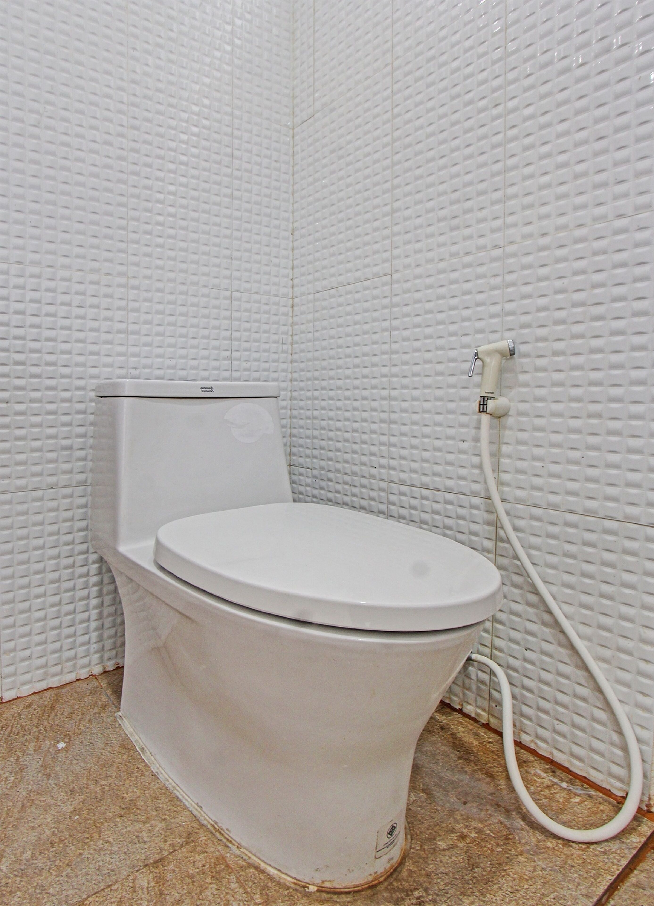 Un inodoro blanco con bidé en un baño con paredes blancas con textura y suelo de baldosas.