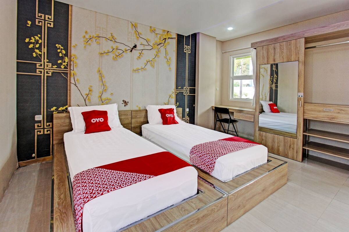 A modern hotel room with two beds, a desk, and a large mirror.