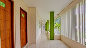 A corridor with wooden doors, green pillars, and a balcony with a white railing. - Capital O 91384 Rintaka Residence (Senggigi)
