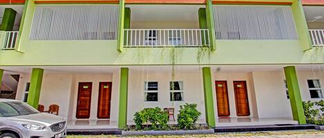 A two-story building with a green and white facade, balconies, and a paved entrance area.