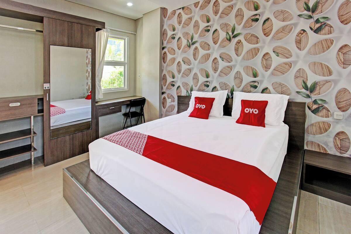 A bedroom with a bed, a desk, a chair, a mirror, and a patterned wall.