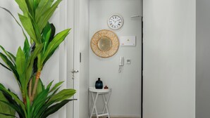 A hallway with a potted plant, a wall clock, a decorative mirror, a small table with a vase, and a wall-mounted thermostat. - Central Light and Bright Studio, No Loadshedding (Cape Town)