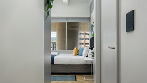 A modern bedroom with a bed, bedside table, and a view of the city through a large window. - Central Light and Bright Studio, No Loadshedding (Cape Town)