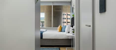 A modern bedroom with a bed, bedside table, and a view of the city through a large window.