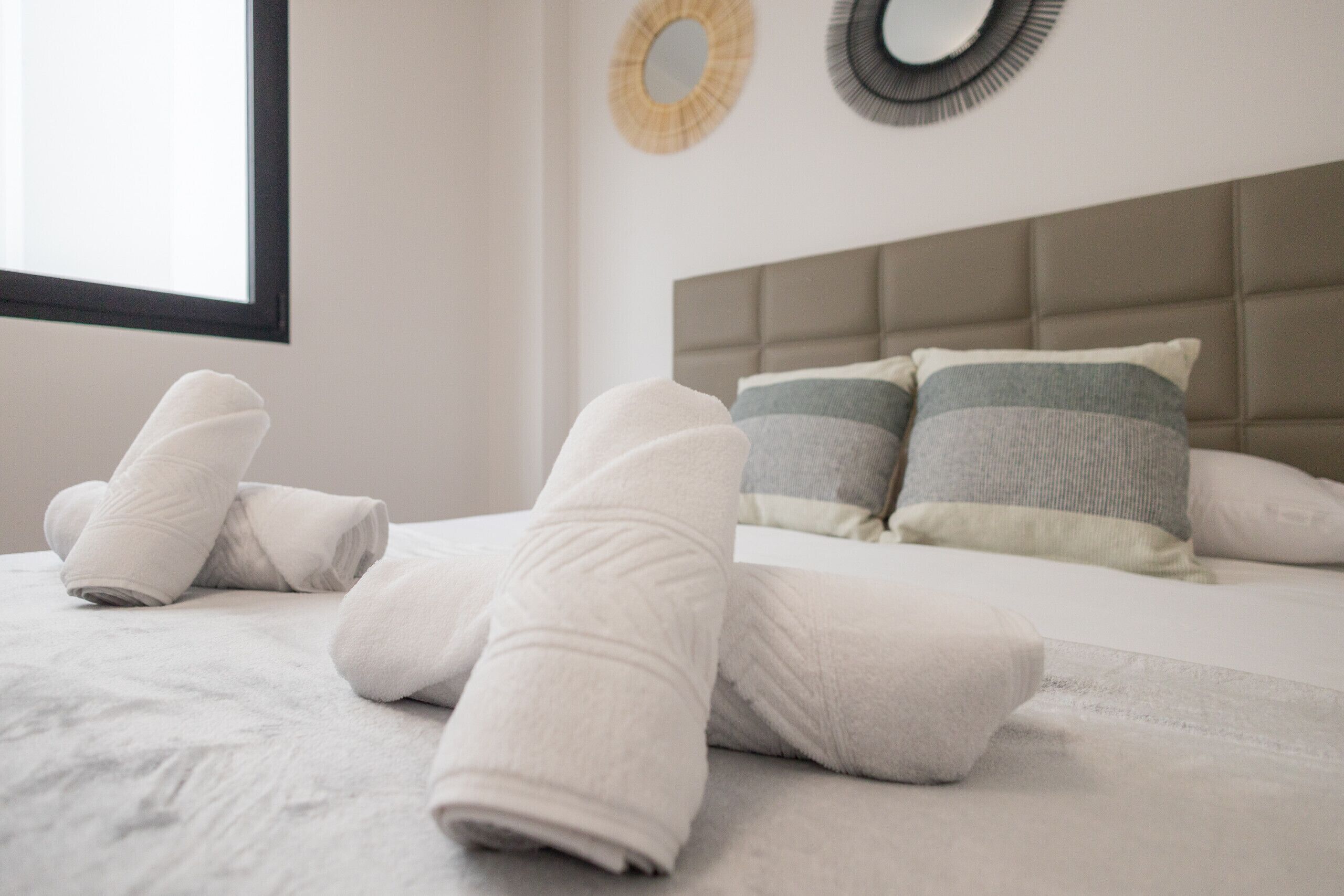 A neatly made bed with white towels, a grey and white striped pillow, and a headboard.