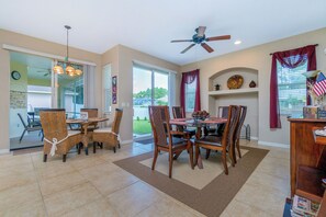 A dining area with a table and chairs, a ceiling fan, and a view of the outdoors.