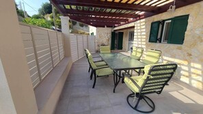 A covered patio with a table and chairs, a stone wall, and a door with green shutters.