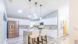 A modern kitchen with white cabinets, stainless steel appliances, and a granite island with bar stools. - Encanto /12 Ppl/ Pool/ Close to Disney Parks/ Games (Clermont)