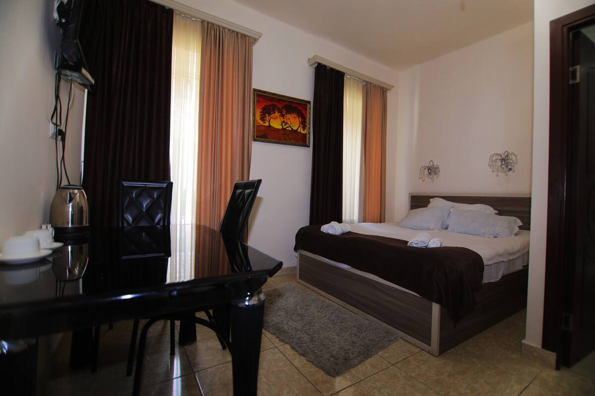 Ein Hotelzimmer mit Bett, Schreibtisch, Stuhl, einer Kaffeemaschine und einem Bild an der Wand.