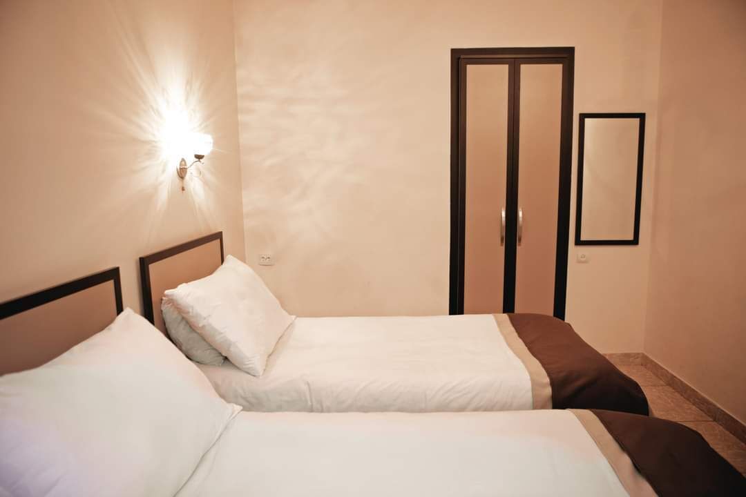 Et hotelværelse med to senge, en lampe på væggen, en dør og et spejl.