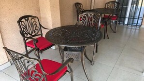 Un espace patio aménagé avec des chaises en métal et une table ronde, dont les chaises et la table présentent des motifs complexes.