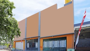 A building with a large orange facade, a closed garage door, and a flag on the right. - OYO 91583 D’cost Green Syariah (Sidoarjo)