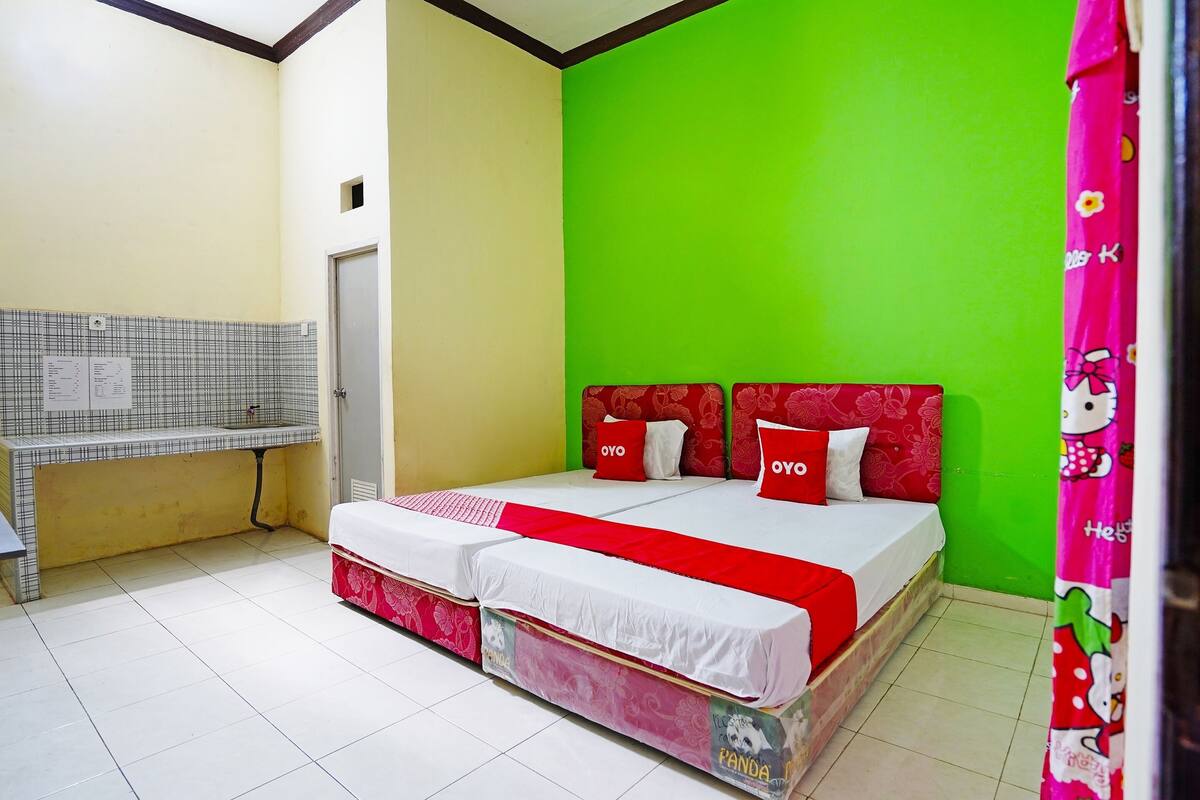 Una habitación con dos camas, un banco, una pared verde y una puerta blanca.