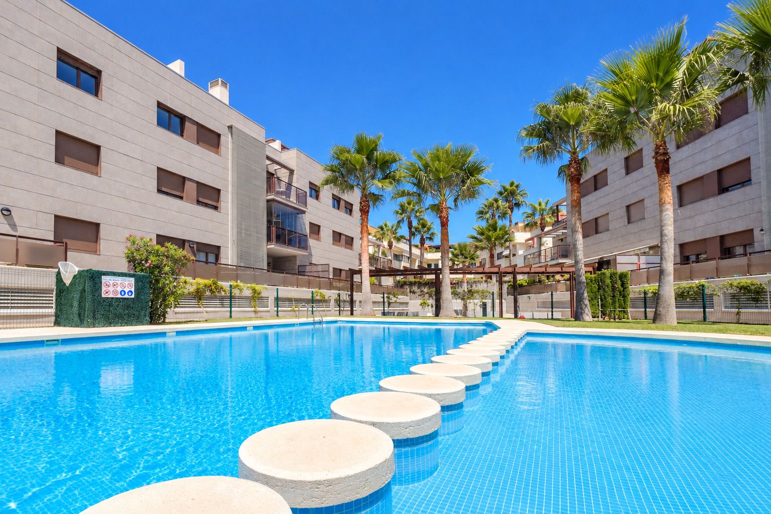 A swimming pool with steps leading into it, surrounded by palm trees and modern buildings.