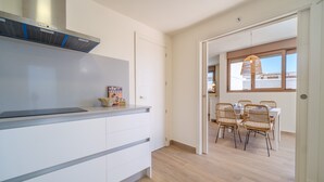 Una cocina moderna con armarios blancos, horno empotrado y una zona de comedor con sillas de mimbre y una mesa.