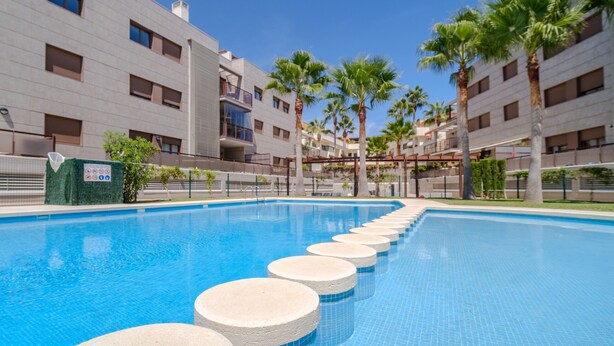 Una piscina con escalones circulares para acceder a ella, rodeada de edificios modernos y palmeras.