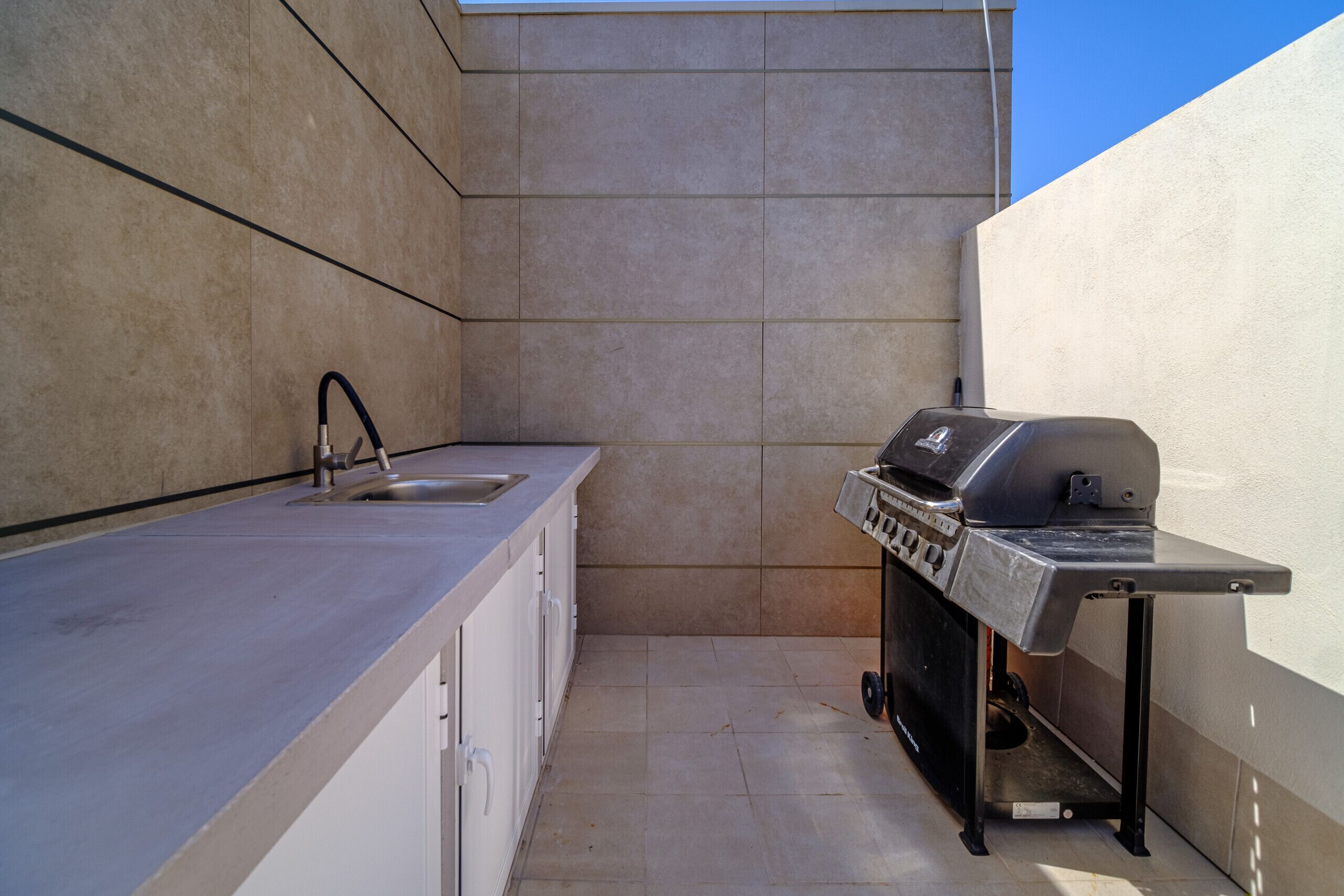 A compact kitchen with a sink, a built-in grill, and a tiled backsplash.