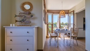 Un comedor con una mesa y sillas, un armario blanco con cajones y una pieza de decoración con motivos de peces en la pared.
