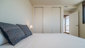 Un dormitorio con una cama, almohadones estampados, una lámpara de noche y un ventanal corredero que da a un balcón.