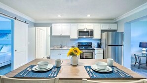 Una cocina moderna con armarios blancos, electrodomésticos de acero inoxidable y un comedor con una mesa de madera preparada para dos personas.