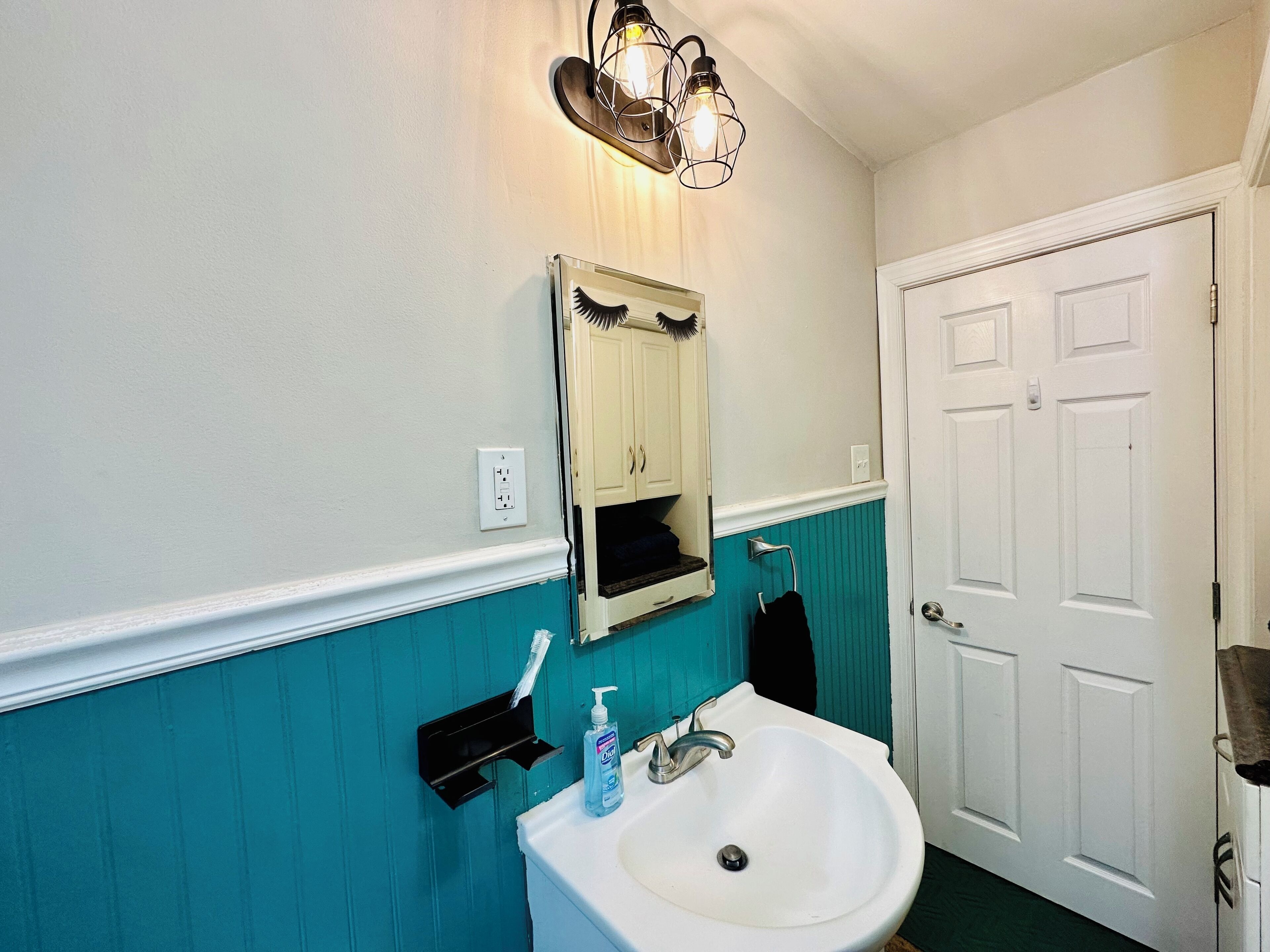 A bathroom with a white sink, a mirror, and a teal wall.