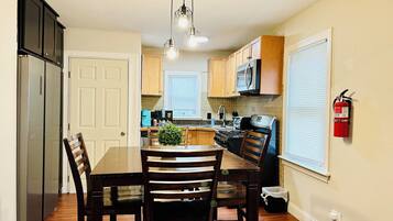 A kitchen with wooden cabinets, a stainless steel refrigerator, a microwave, and a stove. There is a dining table with chairs and a hanging light fixture.