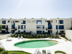 Een modern meerlaags gebouw met een zwembad, terras en een verzorgde tuin.