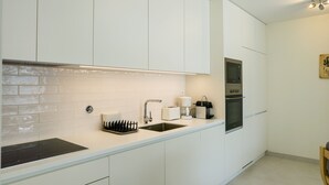 Une cuisine moderne avec des meubles blancs, une cuisinière noire et un four encastré.