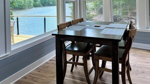 Uma área de refeições com mesa e cadeiras, janelas amplas com vista para um lago e uma decoração de chifres de madeira na parede.