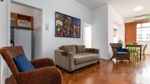 A living room with a sofa, two wicker chairs, a dining table with chairs, a microwave, and a refrigerator.