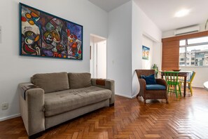 Una sala de estar con un sofá, una silla de mimbre, una mesa de comedor con sillas y un cuadro abstracto grande en la pared.