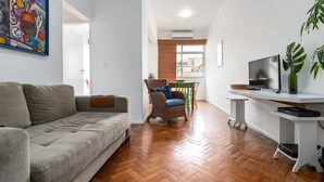 A living room with a sofa, a wicker chair, a TV stand, and a potted plant.