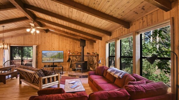Interior acogedor de una cabaña con paredes de madera, chimenea, ventana grande y sofá rojo.