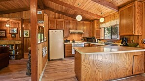 Interior de una cabaña de madera con cocina, que incluye armarios de madera, un refrigerador, un microondas y una isla grande.