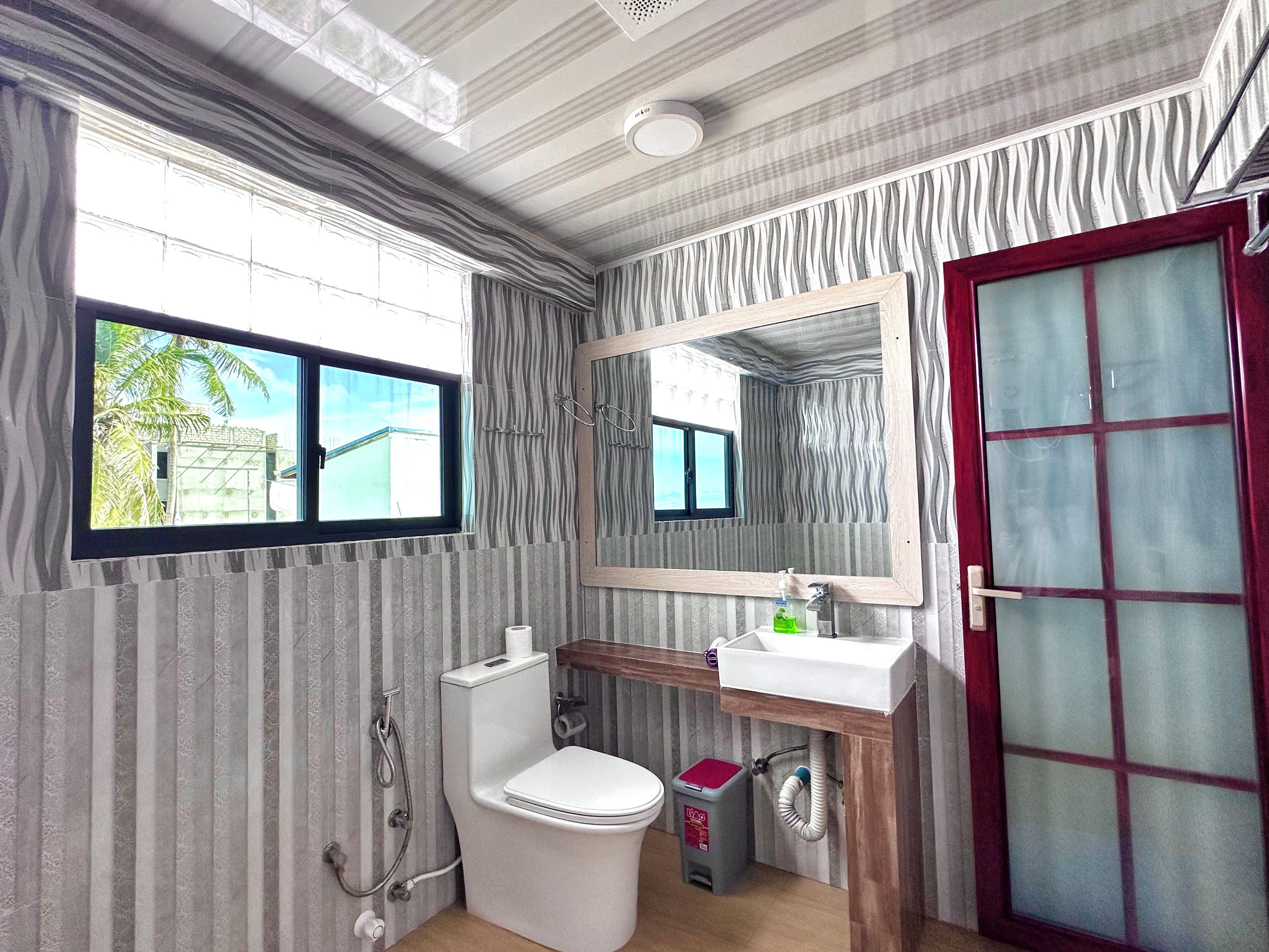 A bathroom with a toilet, sink, mirror, and window.
