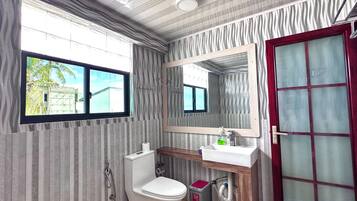 A bathroom with a toilet, sink, mirror, and window.