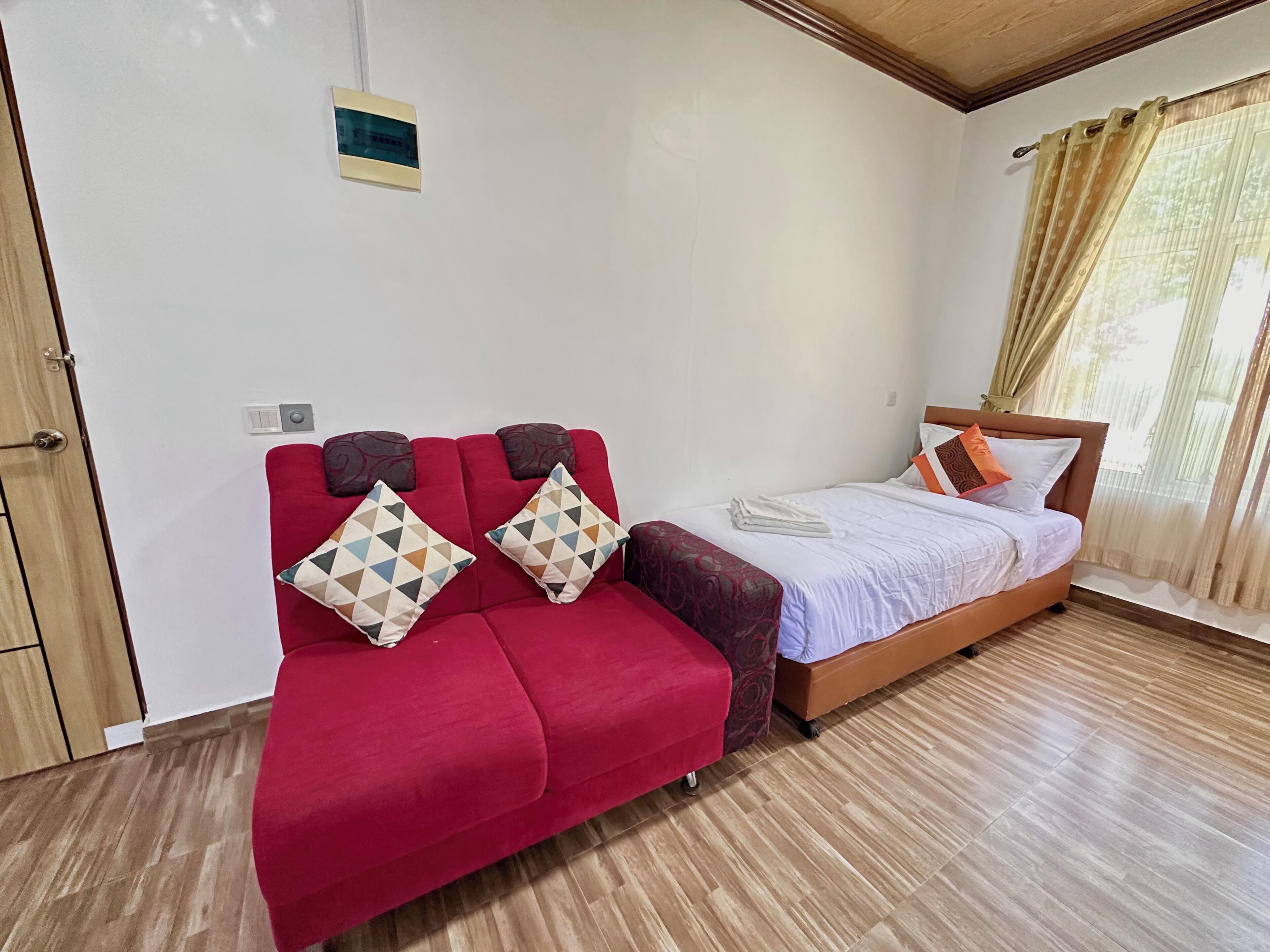 Ein Hotelzimmer mit rotem Sofa, Holzboden, Bett mit weißer Bettwäsche und einem Vorhangfenster.