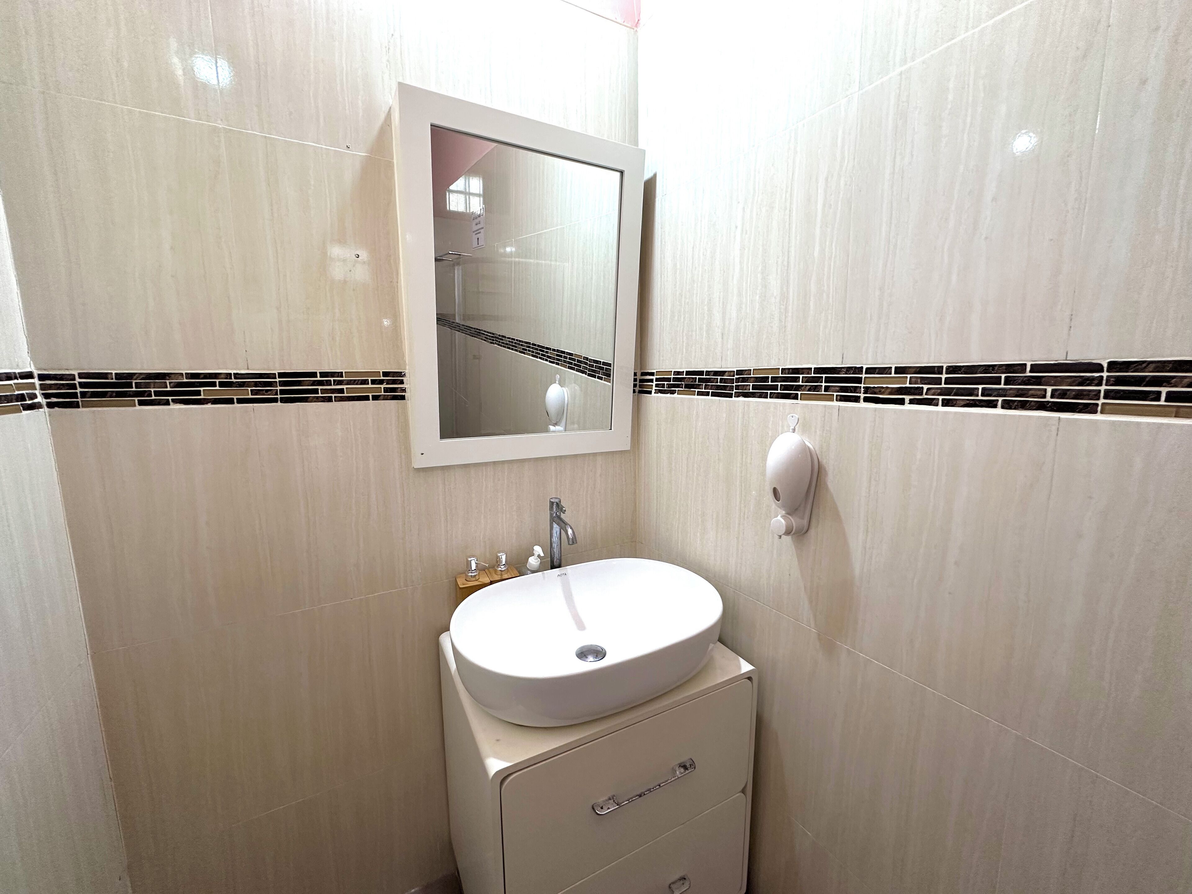 Un baño con lavamanos blanco, un espejo y dispensador de jabón.