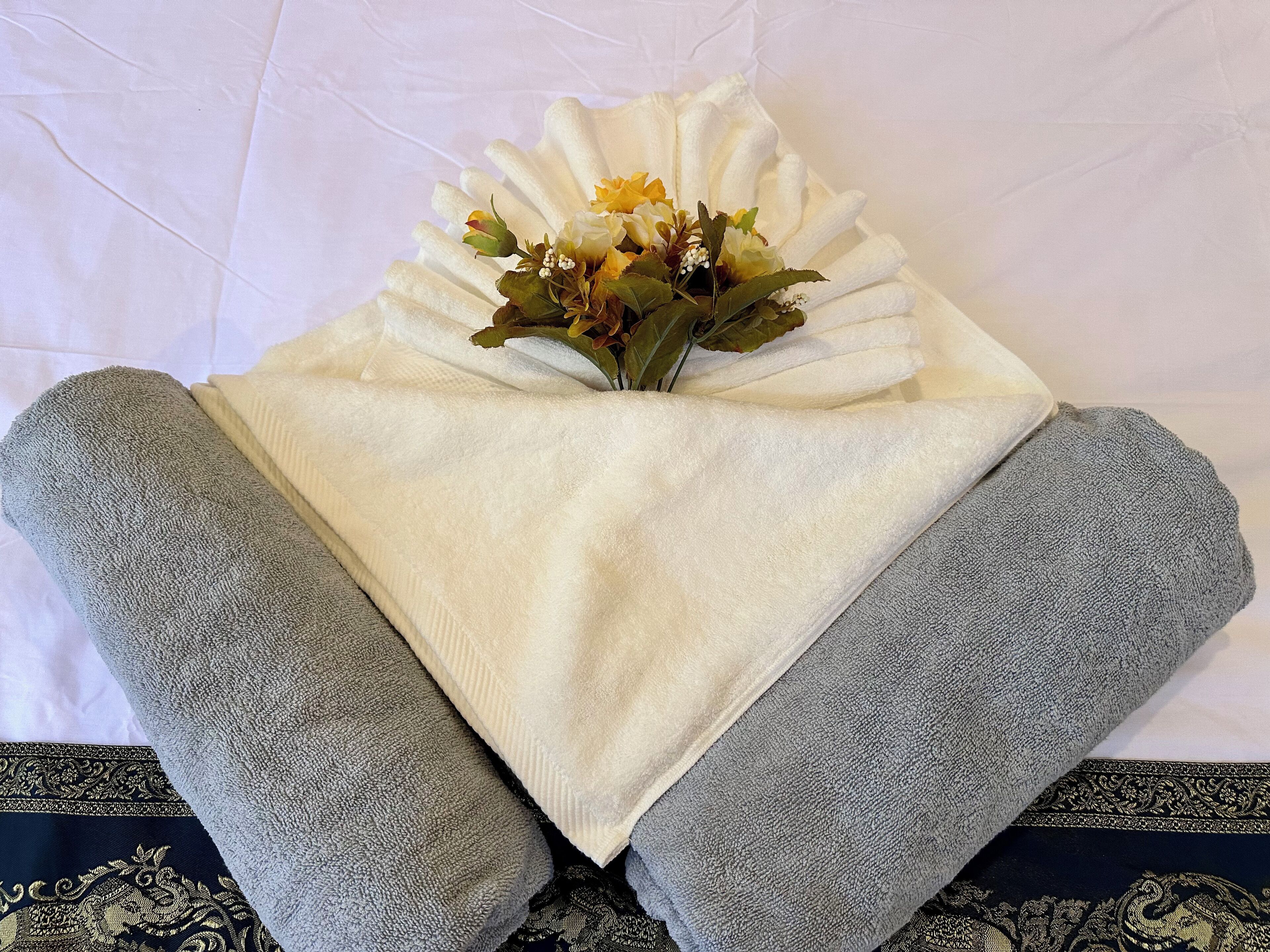 A neatly folded white towel with a bouquet of flowers on a bed.