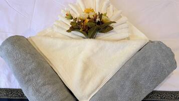 A neatly folded white towel with a bouquet of flowers on a bed.