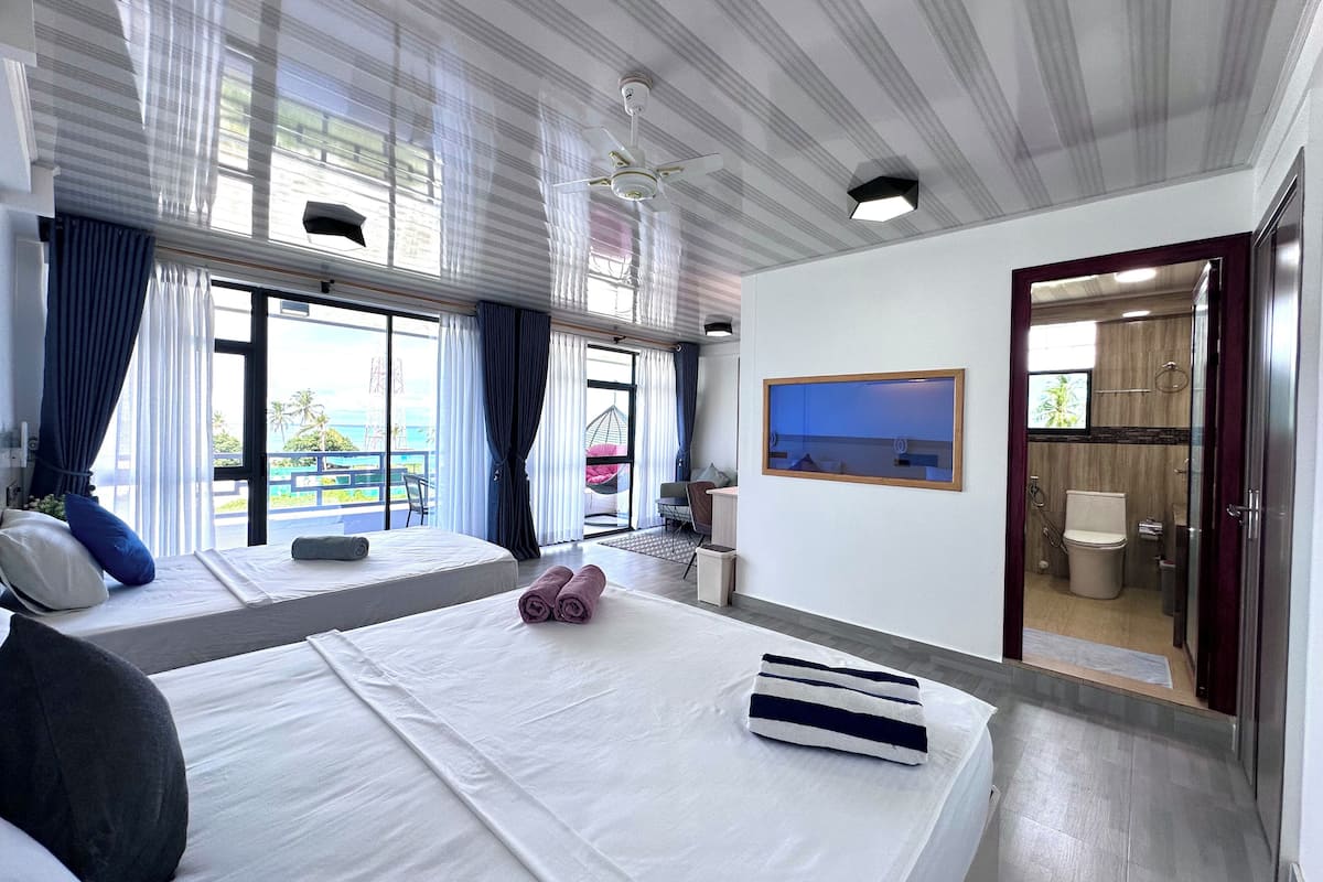 Quarto de hotel com uma cama grande, uma mesa de trabalho, vista para o mar e banheiro.