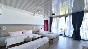Habitación de hotel con dos camas, una puerta roja y vista a la playa.