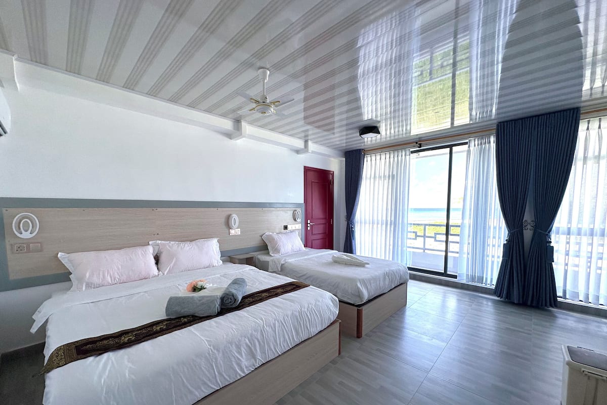 Quarto de hotel com duas camas, uma porta vermelha e vista para a praia.