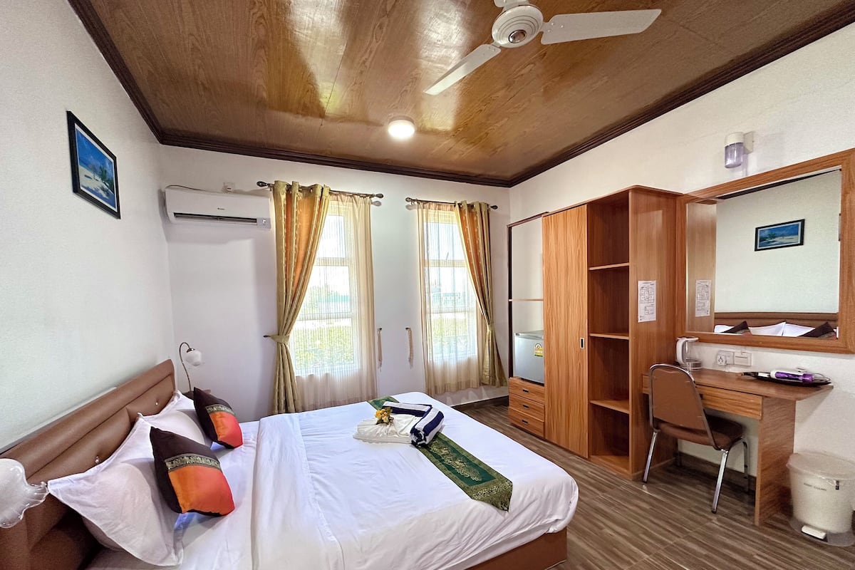 Quarto de hotel com cama, escrivaninha, cadeira, guarda-roupa e ventoinha no teto.
