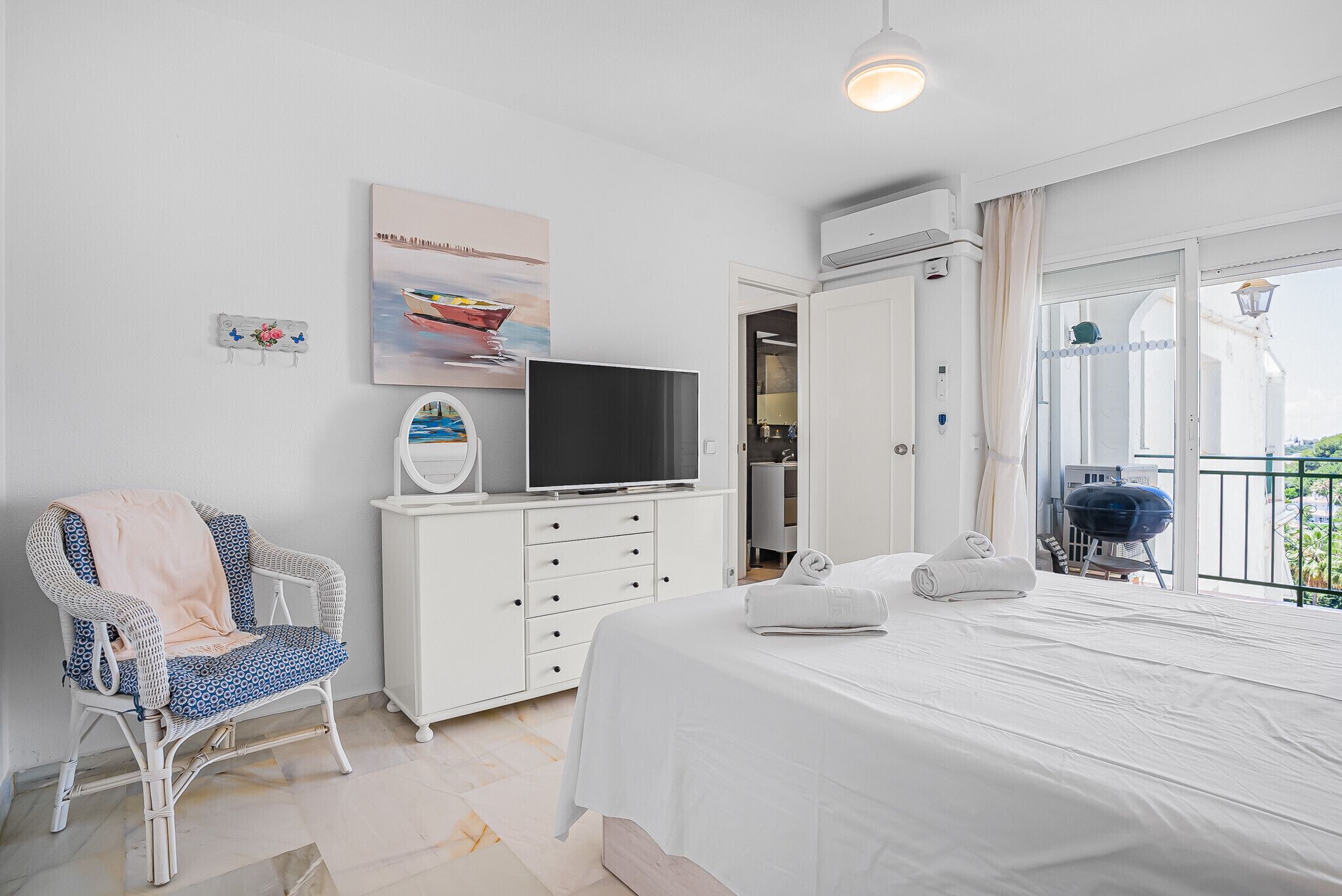 A bedroom with a bed, a TV, a chair, a wardrobe, and a balcony with a grill.