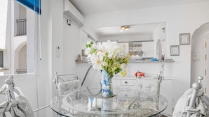 A modern kitchen with white cabinets, a glass dining table, and a vase of white flowers. - P08 Mirador - Apartment (Sitio de Calahonda)