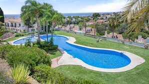 A swimming pool with a curved design, surrounded by well-maintained grass and palm trees. - P08 Mirador - Apartment (Sitio de Calahonda)